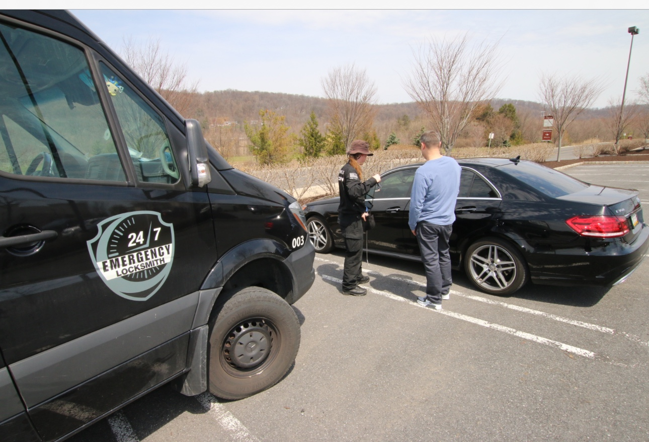 24/7 Emergency Locksmith technician helping a customer beside a car and branded service van